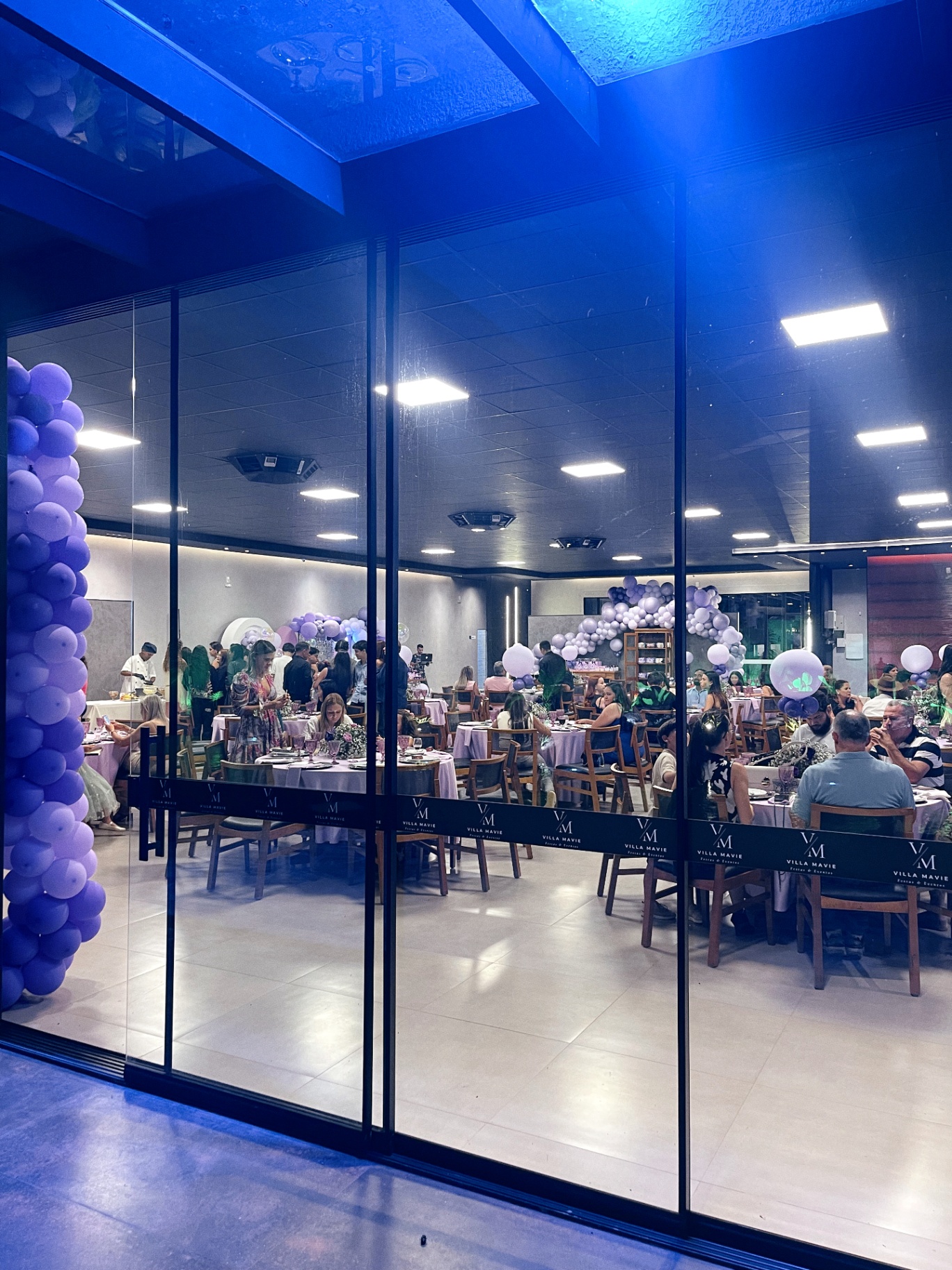 Vista do salão em evento com convidados e decoração lilás